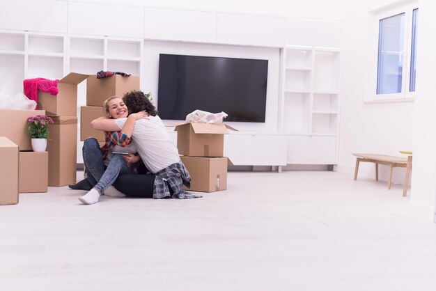 Détente dans une nouvelle maison. Enthousiaste jeune couple assis sur le sol tandis que des boîtes en carton s'étendent tout autour d'eux