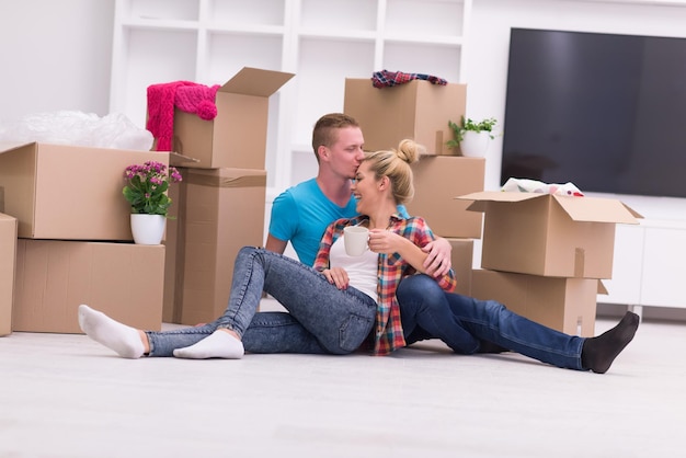 Détente dans une nouvelle maison. Enthousiaste jeune couple assis sur le sol tandis que des boîtes en carton s'étendent tout autour d'eux