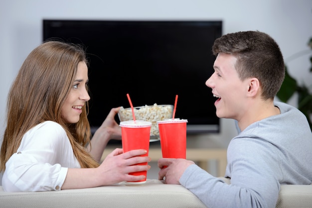 Détente jeune couple devant la télé et buvant du cola.