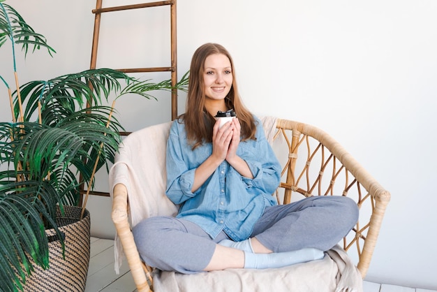 Détente matinale Une fille est assise sur une chaise en osier et savoure un café dans une maison confortable