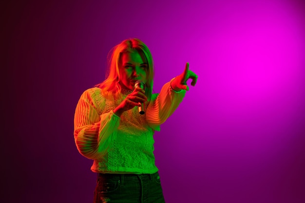 Détente et passe-temps Jeune femme chantant dans un microphone sur fond de studio magenta en néon vert Concept d'émotions lifestyle