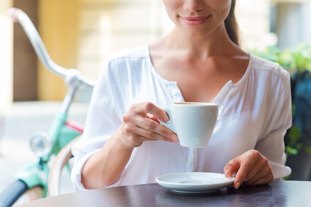 Détente avec une tasse de café frais. Gros plan sur une jeune femme séduisante buvant du café assis au café-terrasse