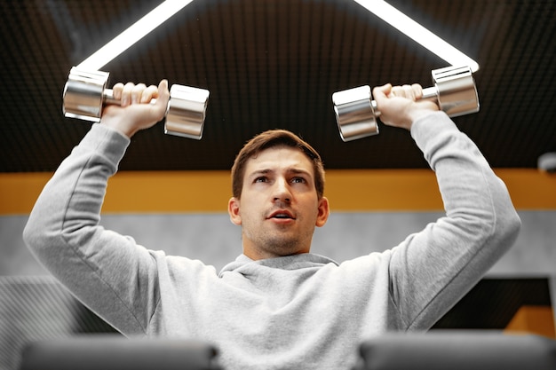 Déterminé beau jeune homme travaillant dans une salle de sport avec des haltères