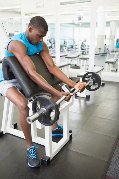 Déterminé jeune homme soulevant des haltères dans la salle de gym