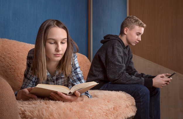 Deux adolescent et fille lisant ensemble à l'intérieur à l'aide d'un téléphone et d'un livre papier.