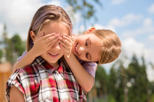 Deux adolescentes assises sur le banc l'une derrière l'autre, une fille fermant les yeux sur l'autre fille.