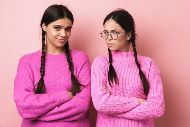 deux adolescentes en colère avec des tresses dans des vêtements décontractés debout avec les bras croisés isolés sur un mur rose