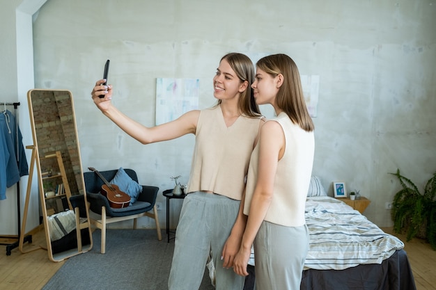 Deux adolescentes heureuses regardant la caméra du smartphone tout en faisant un selfie