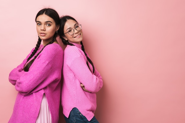 deux adolescentes heureuses avec des tresses dans des vêtements décontractés souriant à la caméra isolée sur un mur rose
