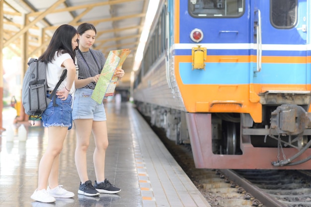 Deux adolescentes regardant une carte pour voyager en train, planifiant un voyage en train, une jeune voyageuse avec une carte debout près du quai du train, regardant la carte, concept de voyage.