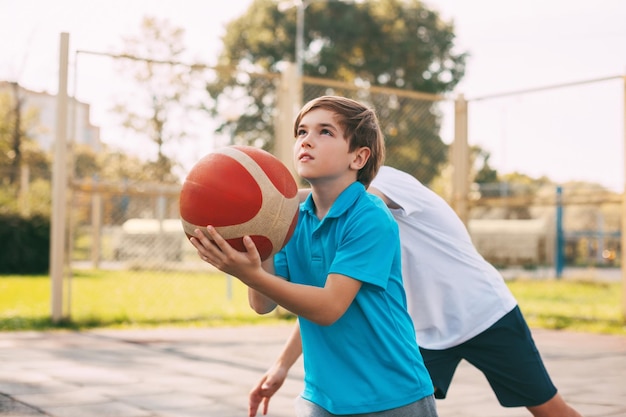 Photo deux adolescents jouent au basket sur le terrain de jeu. les athlètes se battent pour la balle dans le jeu.