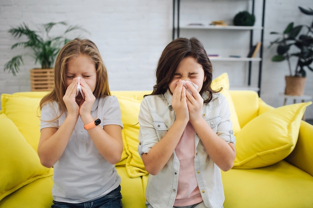 Deux adolescents malades se tiennent dans la chambre et éternuent. Ils tiennent des tissus blancs dans les mains. Les gitls souffrent. Ils sont malades.