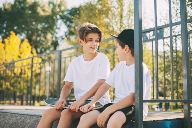 Deux adolescents mignons s'assoient dans un skatepark, se détendent après la planche à roulettes et discutent. Le concept de jeunesse