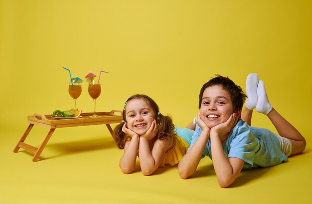 Deux adorables enfants couchés sur fond jaune près d'un plateau en bambou