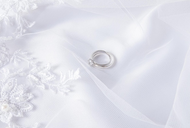 Deux alliances en or blanc avec un diamant reposent sur un voile blanc avec des plis doux Mise en page de fond de mariage pour l'invitation de carte postale de conception