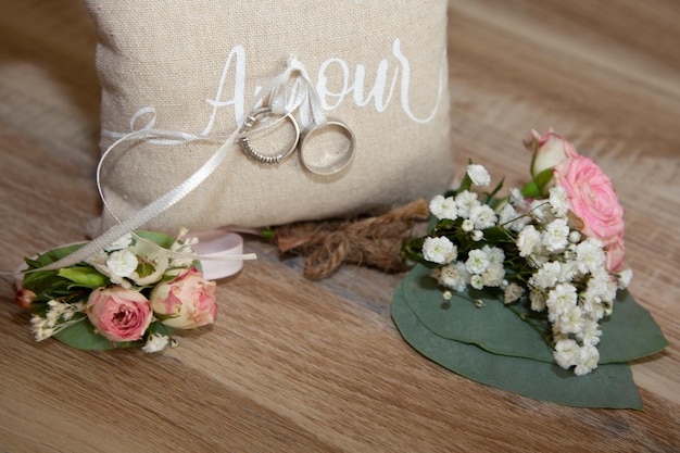 Photo deux alliances sur un oreiller naturel marron avec ruban avec texte d'amour signifie amour en français et décoration de fleurs