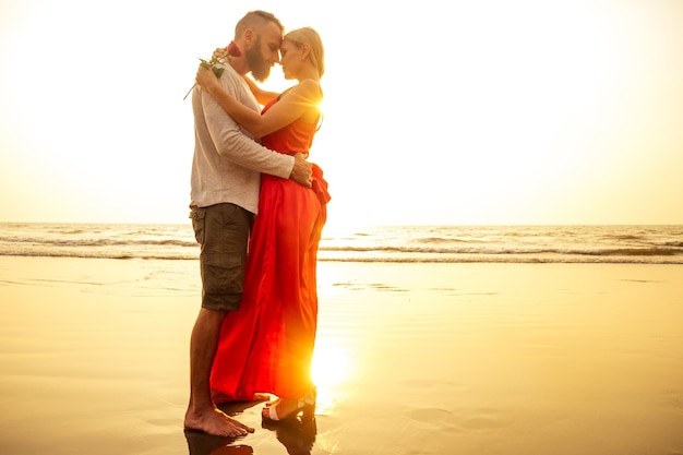 Deux amants au coucher du soleil au bord de la mer sentiments de romance et de tendresse premier amour dateman et femme blonde vêtue d'une robe sur la plage avec des rayons de soleil rosesSaint Valentin et Journée internationale de la femme