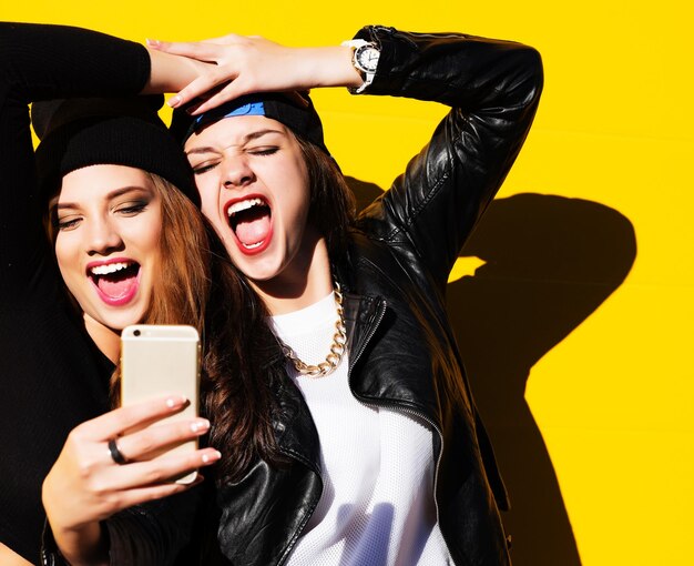 Deux amies adolescentes en tenue hipster à l'extérieur font un selfie sur un téléphone