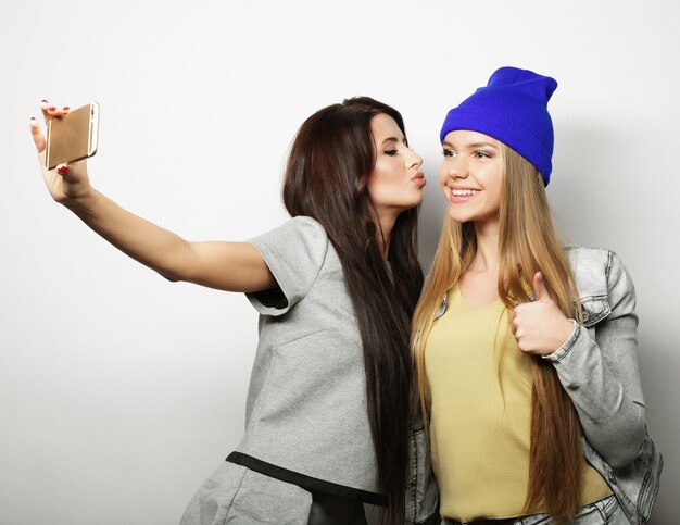 Deux amies adolescentes en tenue hipster font selfie sur fond blanc