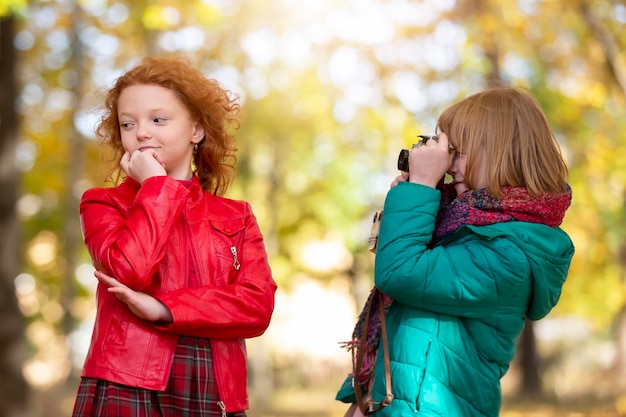 Deux amies aux cheveux roux se photographient dans le parc d'automne avec un appareil photo rétro