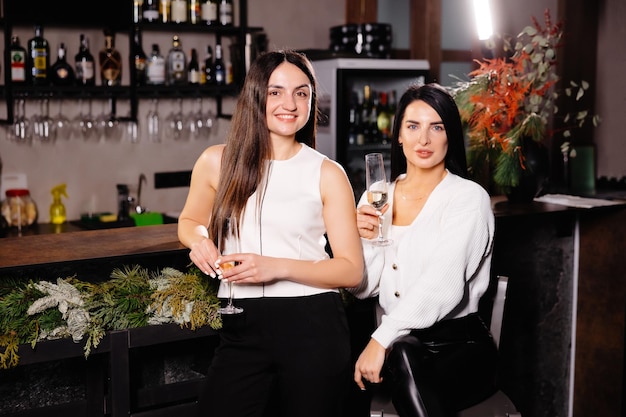 Deux amies caucasiennes heureuses buvant et parlant assis à une table dans le bar d'une discothèque