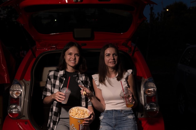 Deux amies avec du pop-corn assis dans la voiture tout en regardant un film en voiture au cinéma Mise au point sélective Divertissement activités de loisirs concept de passe-temps