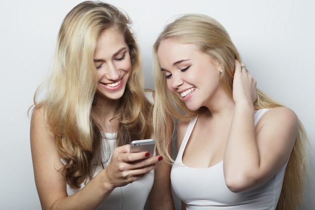 Deux amies heureuses partageant les médias sociaux dans un téléphone intelligent, sur fond gris