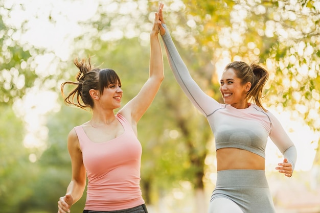 Deux amies heureuses portant des vêtements de sport font du jogging ensemble dans la nature par une journée ensoleillée.