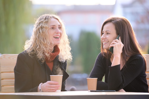 Deux amies heureuses s'amusant ensemble au café de la rue en riant et en parlant au téléphone portable.