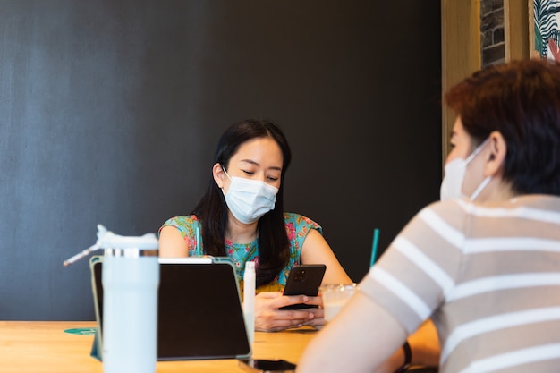 Deux amies ih masque de protection assis sur un café à la recherche d'un téléphone portable