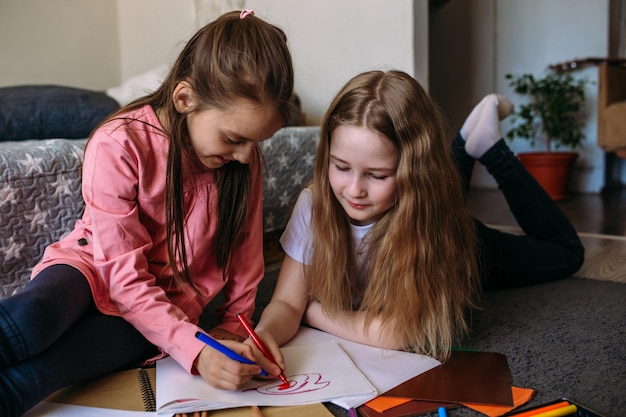 Photo deux amies jouent à la maison, dessinent avec des crayons et des stylos et s'amusent.