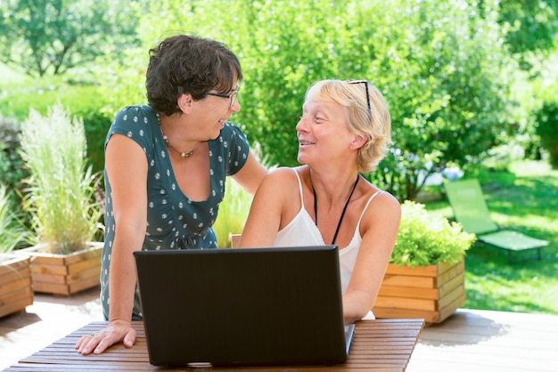 Deux amies matures utilisant un ordinateur portable, sur la terrasse du jardin