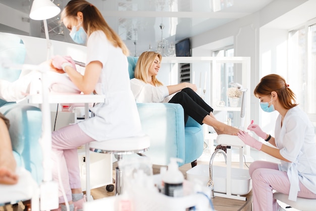 Deux amies sur la procédure de pédicure dans un salon de beauté. Esthéticiennes professionnelles et clientes, soins des ongles en studio spa