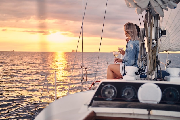 Deux amies se détendant sur le yacht avec des verres de vin dans les mains, au coucher du soleil en haute mer.