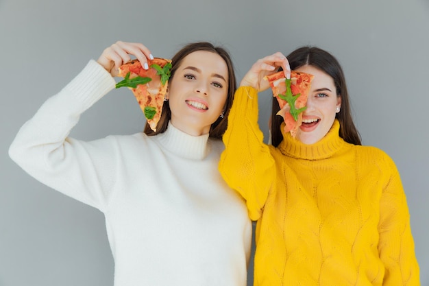 Deux amies tenant des tranches de pizza. Les jeunes s'amusent à dîner.