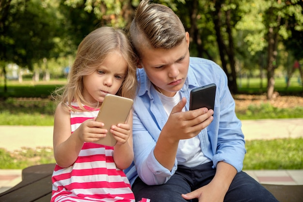 Deux amis adolescents heureux utilisant un téléphone portable tout en se relaxant dans le parc