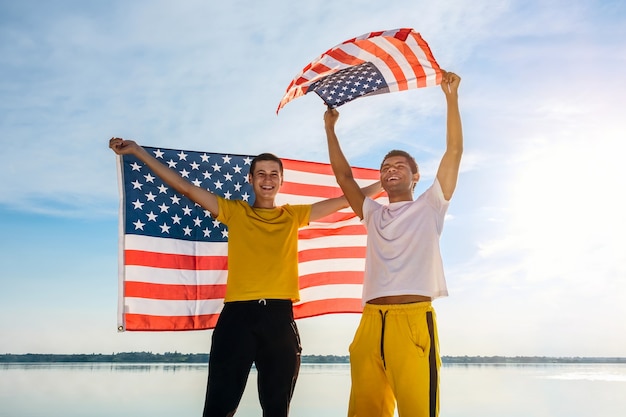 Deux amis afro-américains et caucasiens souriants tenant un drapeau américain