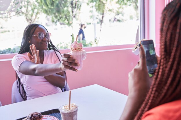 Deux amis afro-américains une femme prend une photo de l'autre tout en montrant un milkshake