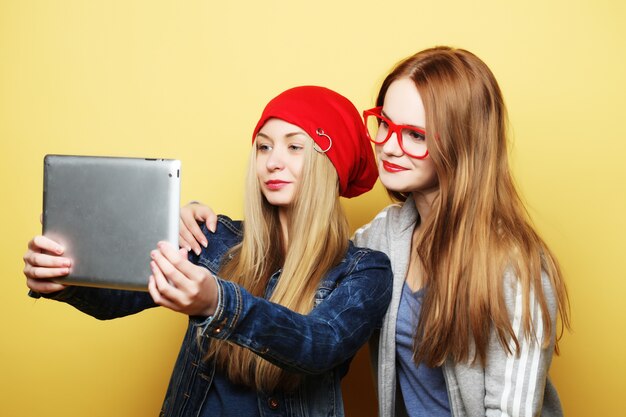 Deux amis filles hipster prenant selfie avec tablette numérique sur jaune