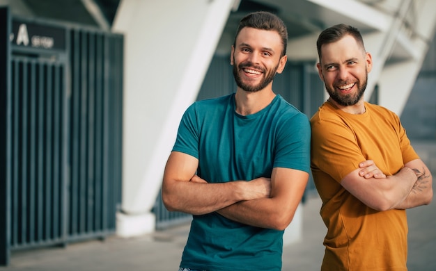 Deux amis ou frères heureux en t-shirts colorés se tiennent dos à dos avec les bras croisés à l'extérieur