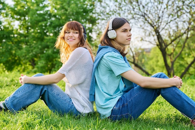 Deux amis gars fille écoutent de la musique podcast dans des écouteurs sans fil assis sur l'herbe