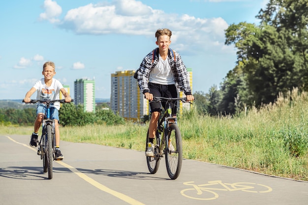 Deux amis heureux en vêtements décontractés faisant du vélo ensemble sur une piste cyclable dans le parc par une journée ensoleillée