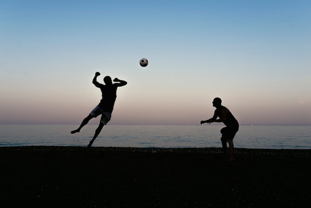 Deux amis jouant au football sur la plage.