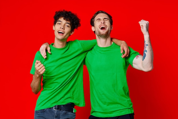 Deux amis joyeux étreignent les émotions de t-shirts verts communication fond rouge