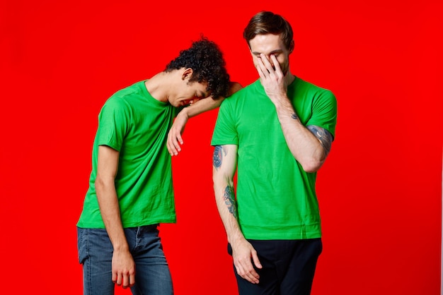 Deux amis joyeux en t-shirts verts joie de communication fond rouge