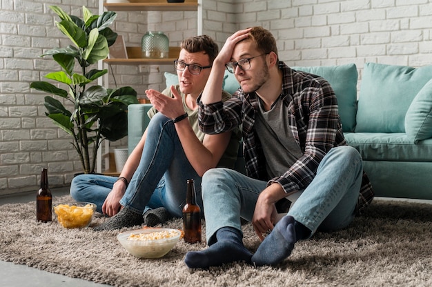 Photo deux amis masculins regardant le sport à la télévision ensemble tout en ayant de la bière et des collations