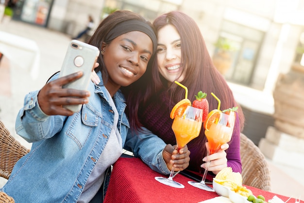 Photo deux amis prenant un selfie tout en acclamant avec des cocktails.