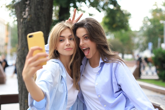 Deux amis riants profitant d'un week-end ensemble et faisant du selfie sur fond de ville.