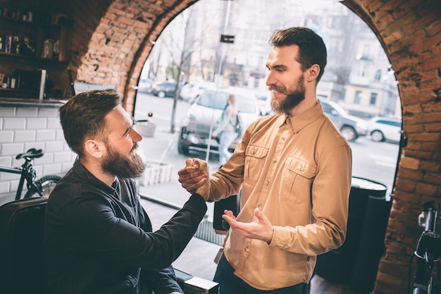 Deux amis sont dans un salon de coiffure. Ils se serrent la main. Les gars se sourient.