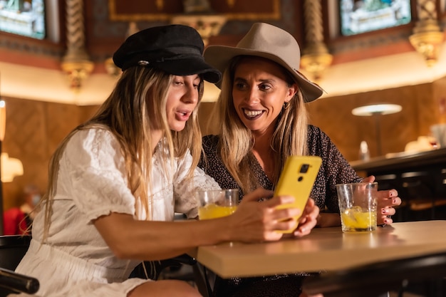 Deux amis touristes regardant au téléphone des activités de loisirs dans une cafétéria moderne. Siroter un jus d'orange, style de vie